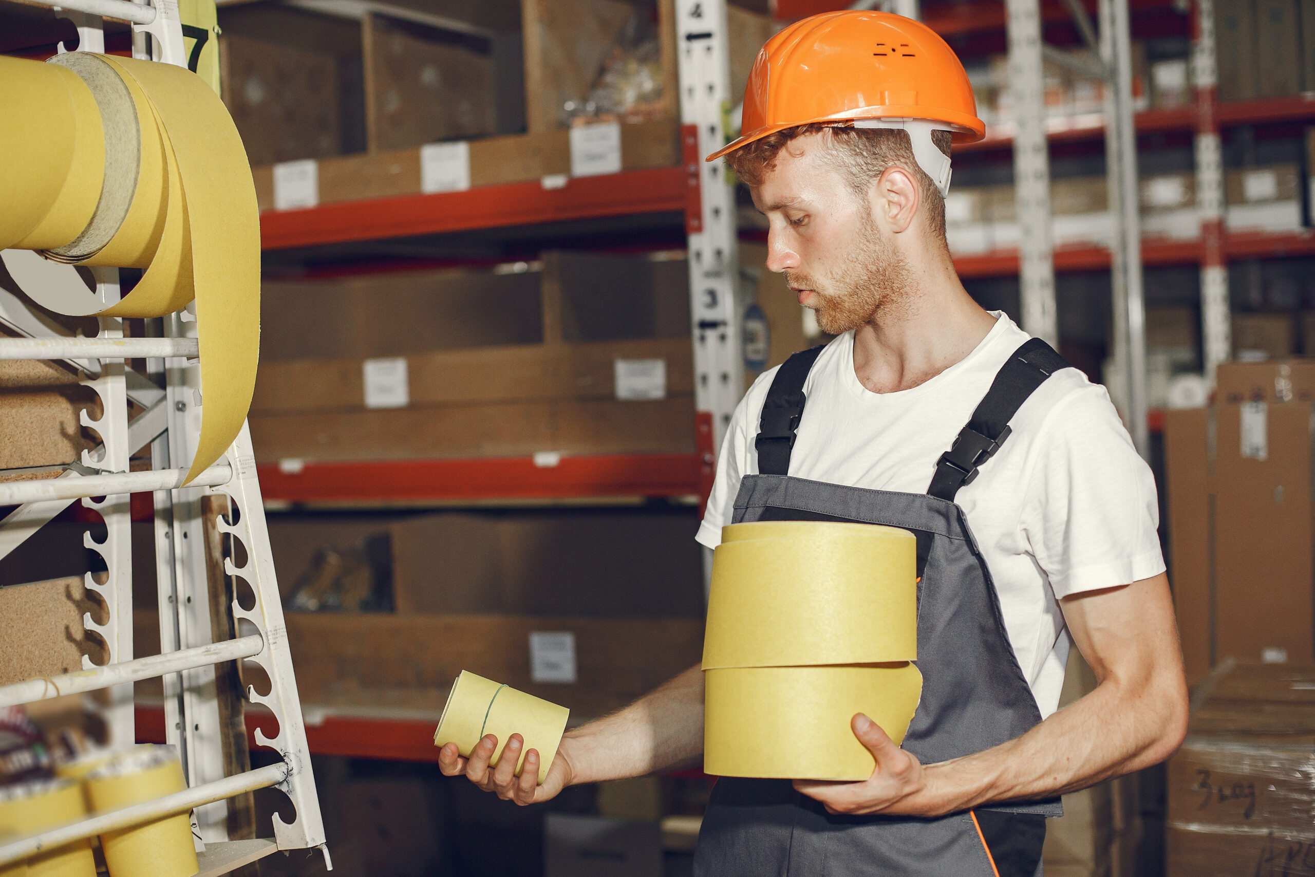 Industrial worker indoors in factory. Young technician with orange hard hat.